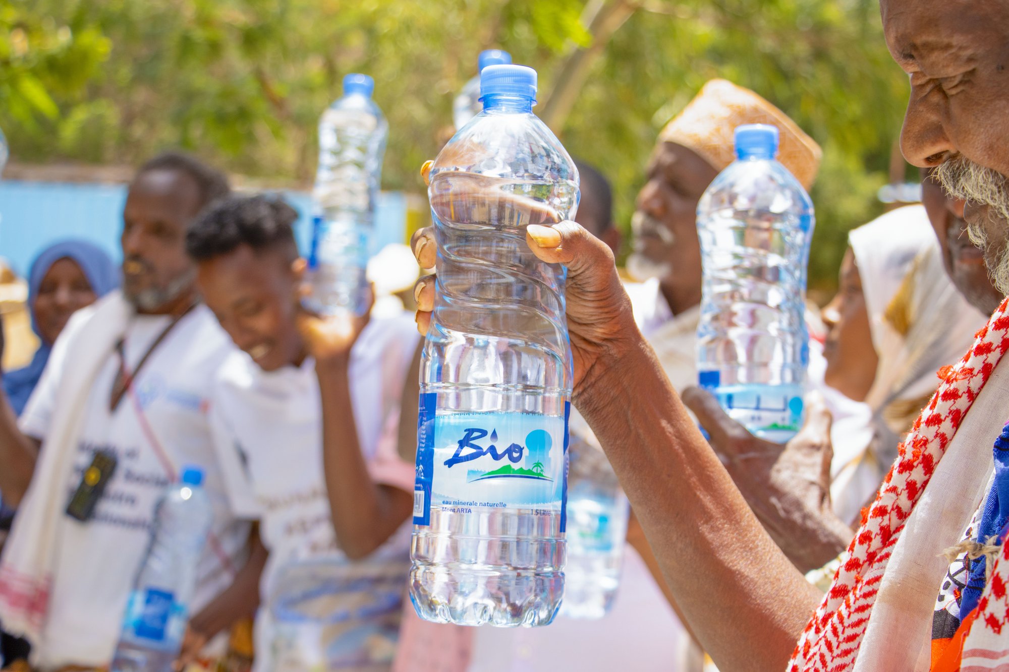 Un membre de la communauté d'Arta tenant une bouteille d'eau Bio lors d'une distribution